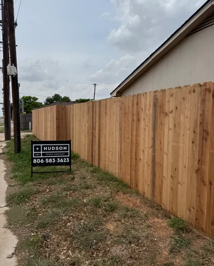 Hudson Fence Company job sign in front of a completed cedar fence and covered patio in Lubbock, TX